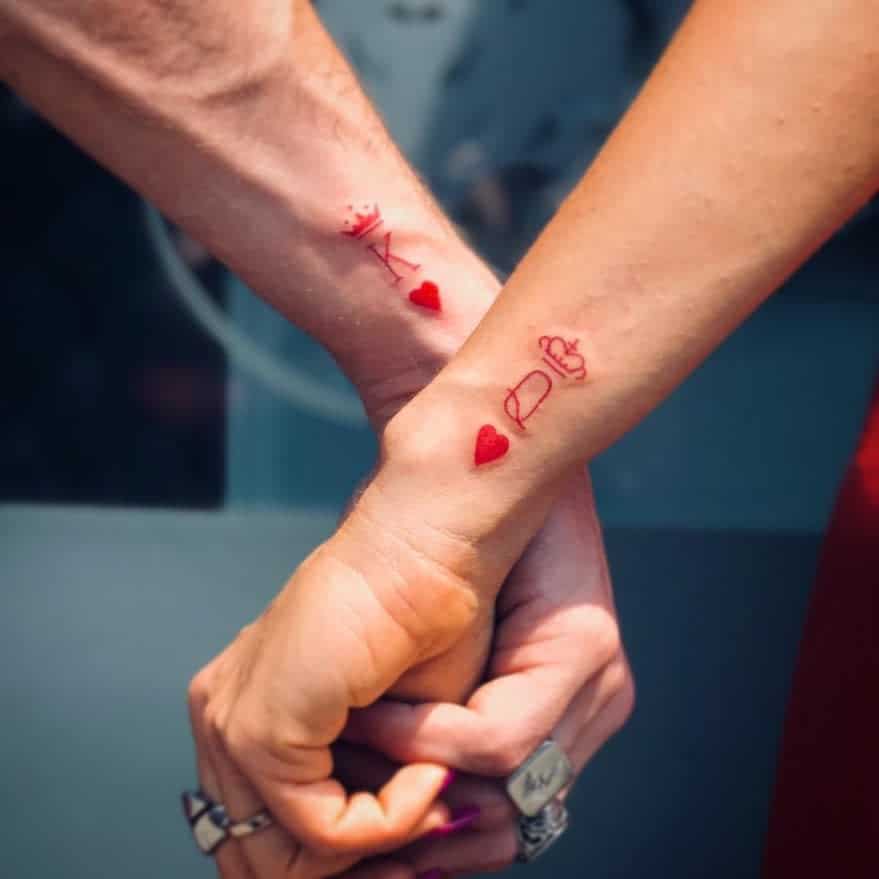 Minimalistic couple's wrist tattoos featuring red Queen and King symbols paired with hearts for a romantic touch