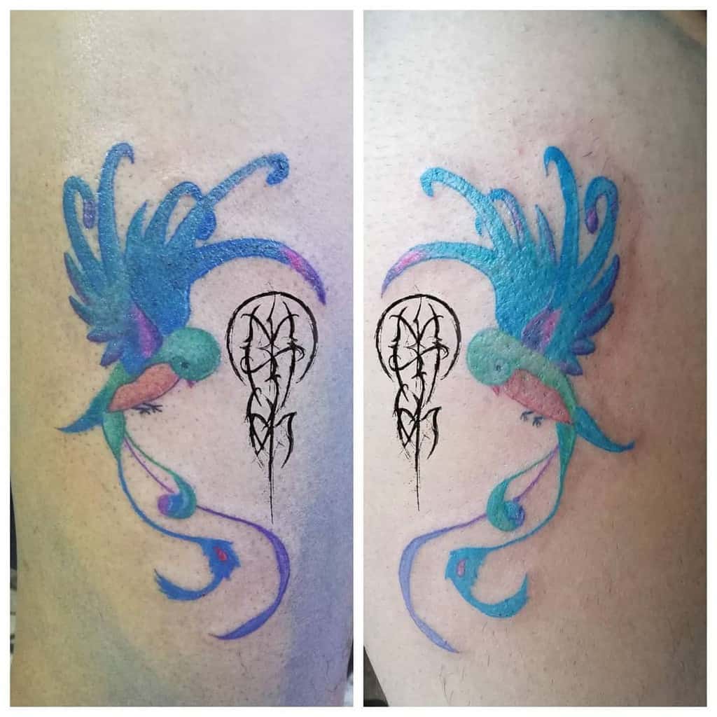 Colorful bird tattoo with flowing feathers and branch design next to a black abstract symbol on skin