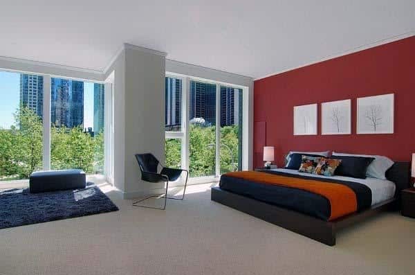 Modern bedroom featuring a striking red accent wall, large windows, and a sleek black chair