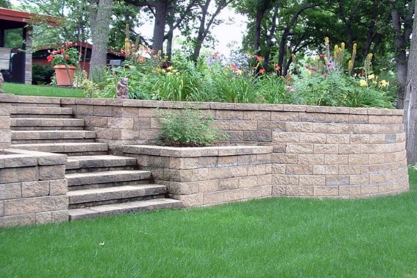 Stone retaining wall with built-in stairs, vibrant flower beds, and a lush green lawn.
