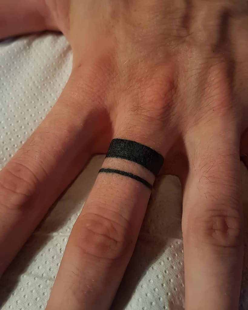 Close-up of a two black bands tattooed on the ring finger