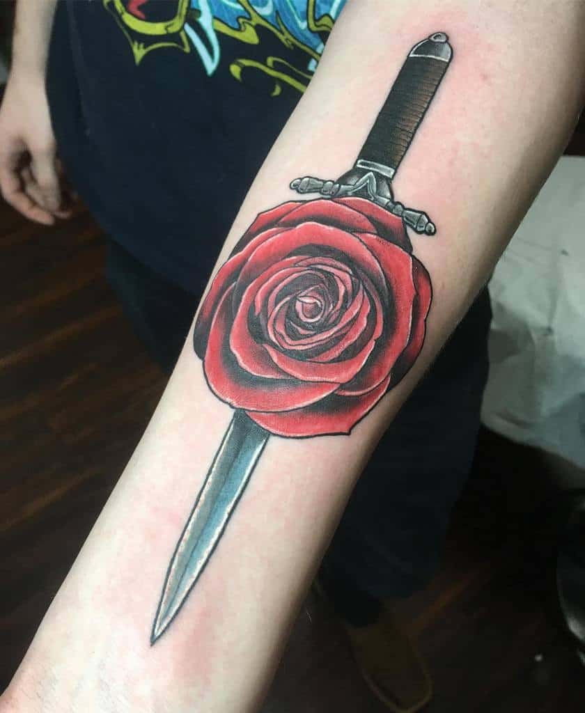 Tattoo of a dagger with a red rose on a forearm