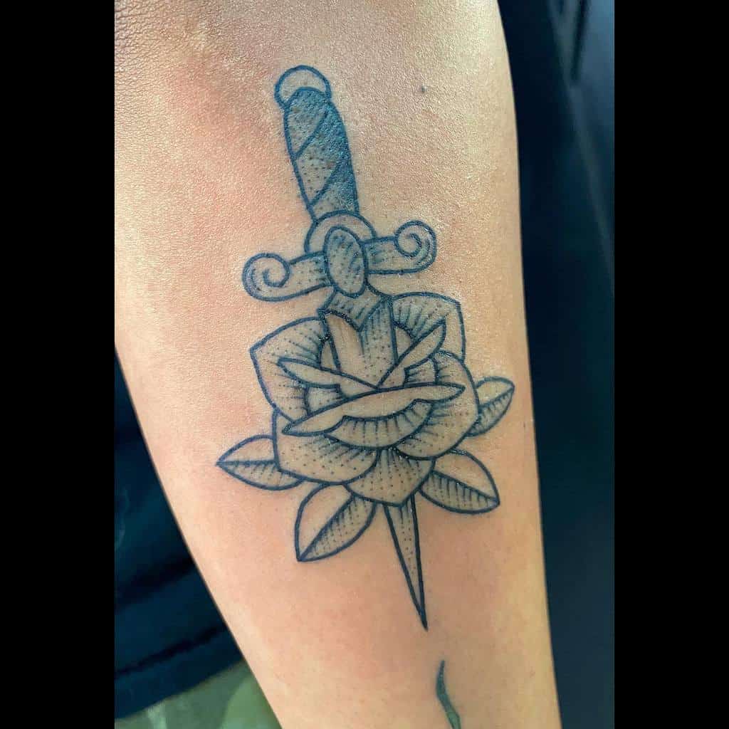 Tattoo of a dagger piercing through a rose on an arm