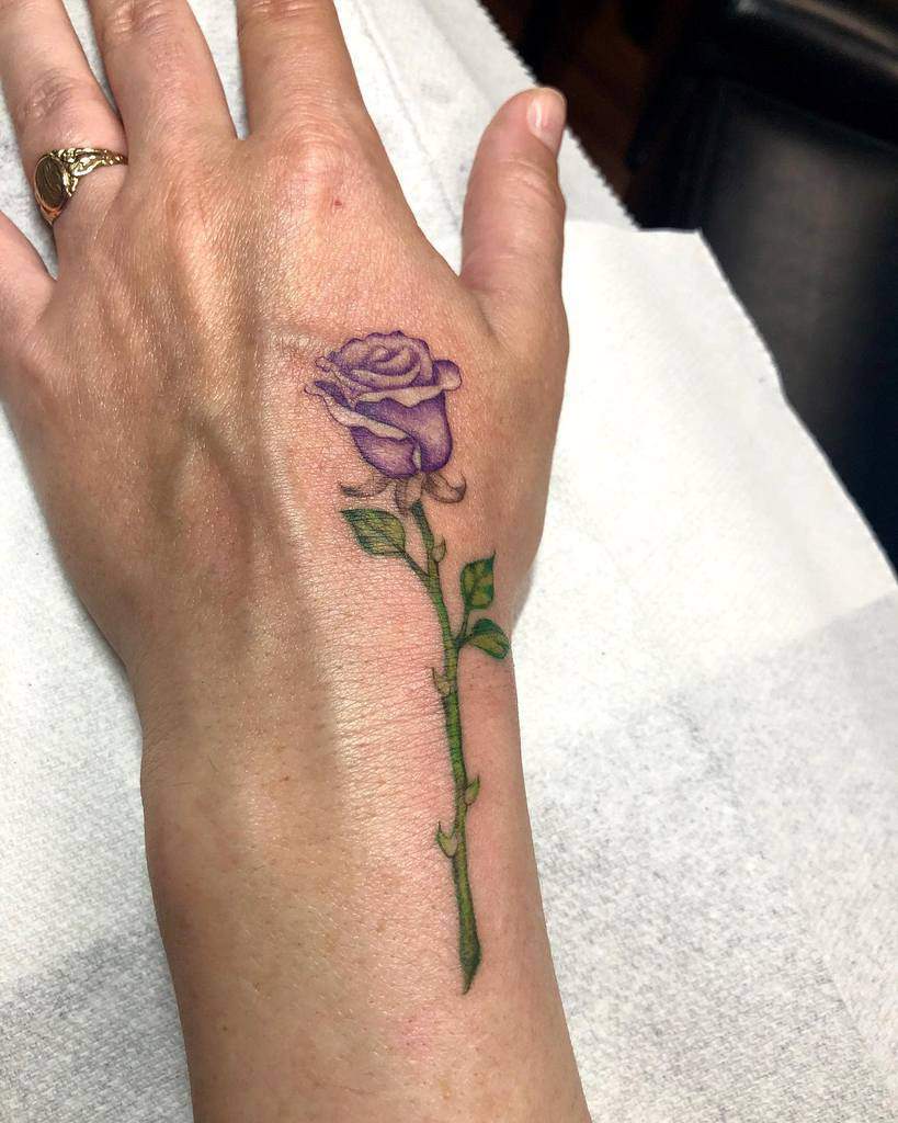 A vibrant purple rose tattoo adorns the back of a hand