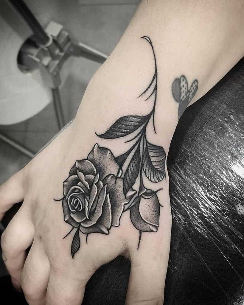 A tattoo of a rose with leaves on a person's hand