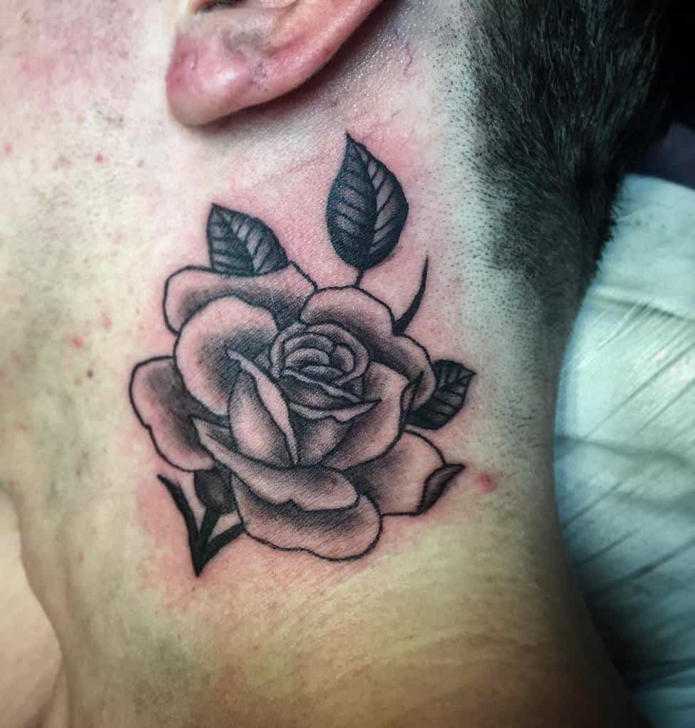 A stunning black and gray rose tattoo elegantly adorns the side of a person's neck, showcasing intricate details and captivating beauty