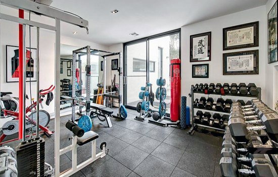 Home gym with rubber flooring, dumbbells, punching bag, weight rack, and framed certificates.