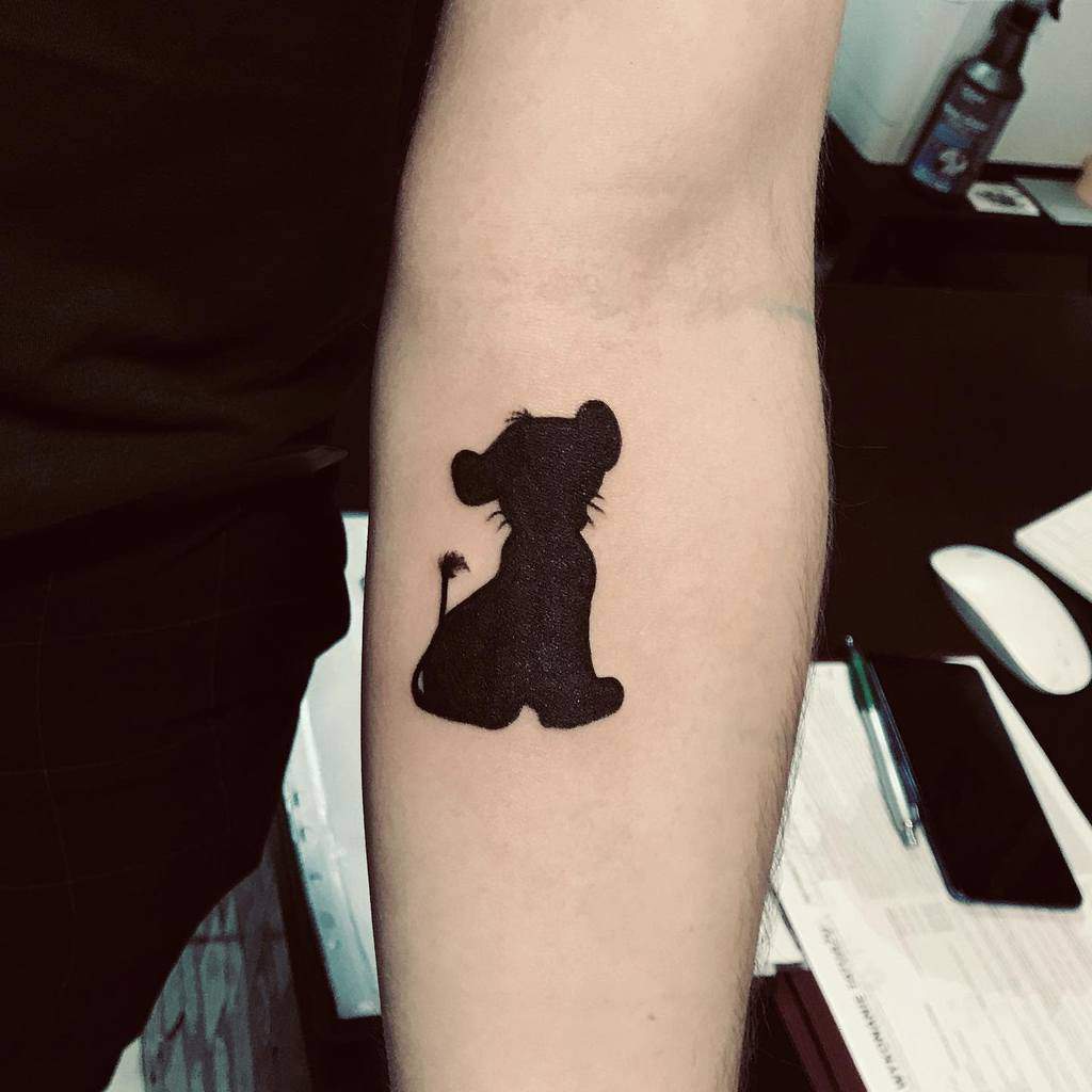 Black silhouette tattoo of a sitting Simba as lion cub