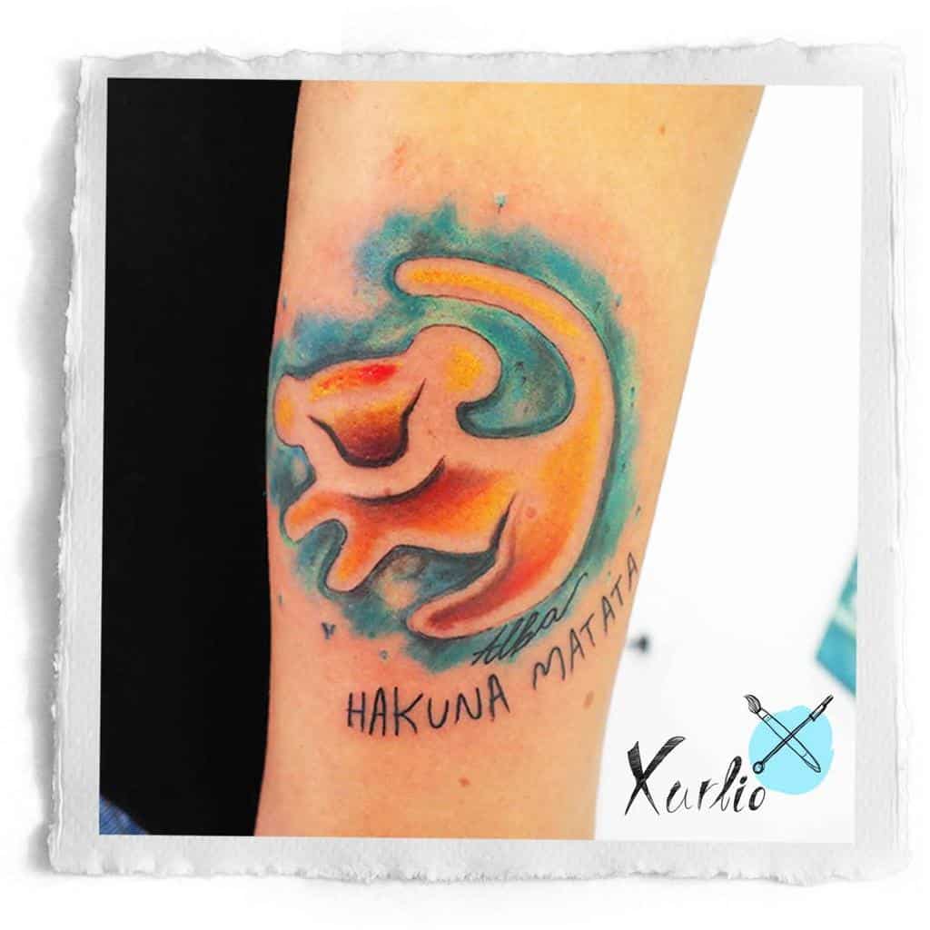Tattoo of an orange Simba as lion cub abstract with blue background, with "Alba Hakuna Matata" text below