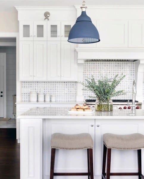 White kitchen with patterned tile backsplash, navy pendant light, and island with bar stools.