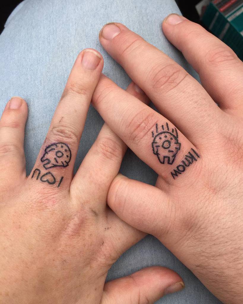 Matching wedding ring tattoos with playful designs, one featuring a heart and the other a smiling figure, with text 'I know' and 'I U' with heart in the middle
