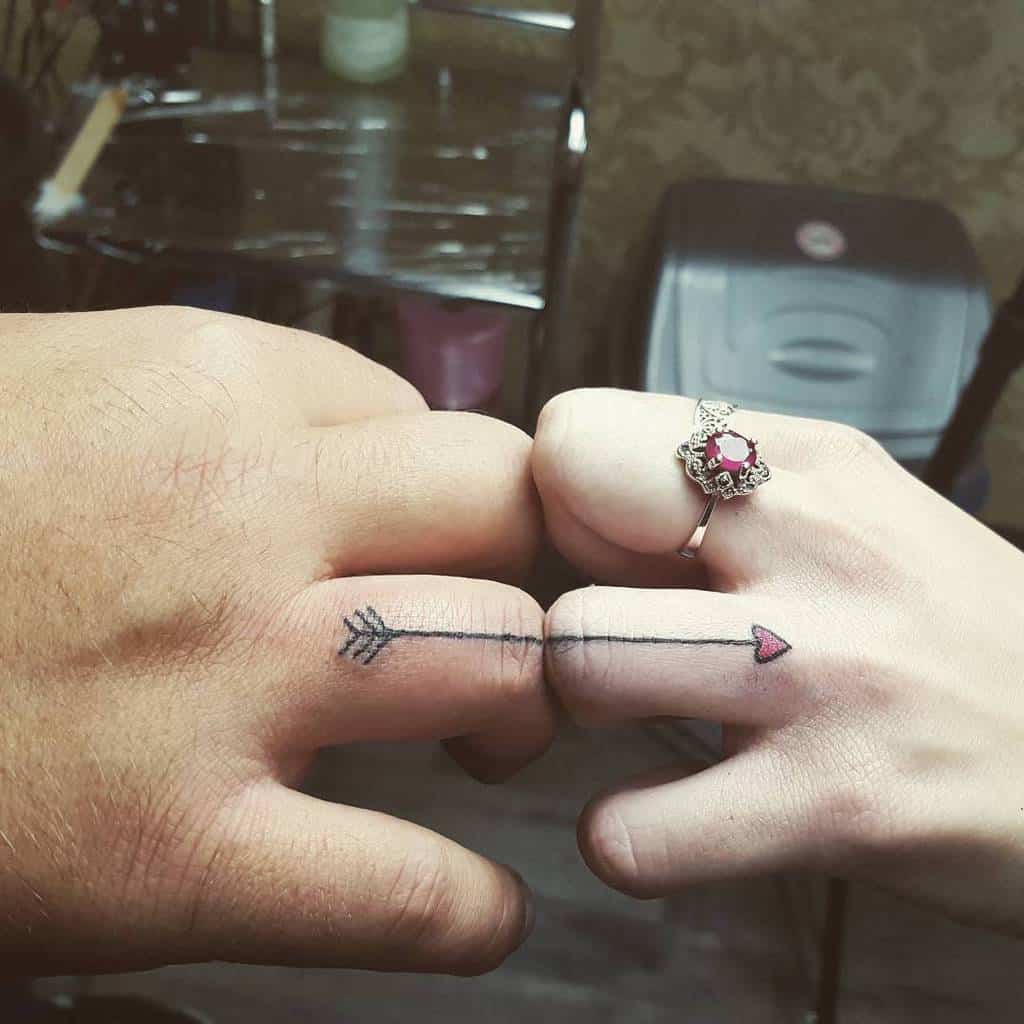 Matching wedding ring tattoos of an arrow design, one with the arrowhead and the other with the heart-shaped tail