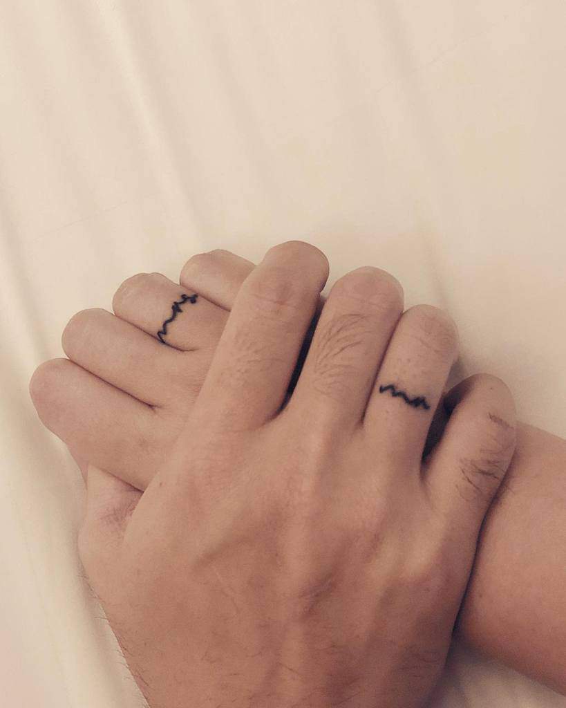 Matching wave-like wedding ring tattoo on the finger, symbolizing unity and connection