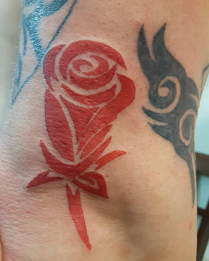 Red abstract rose tattoo beside a black tribal design on skin