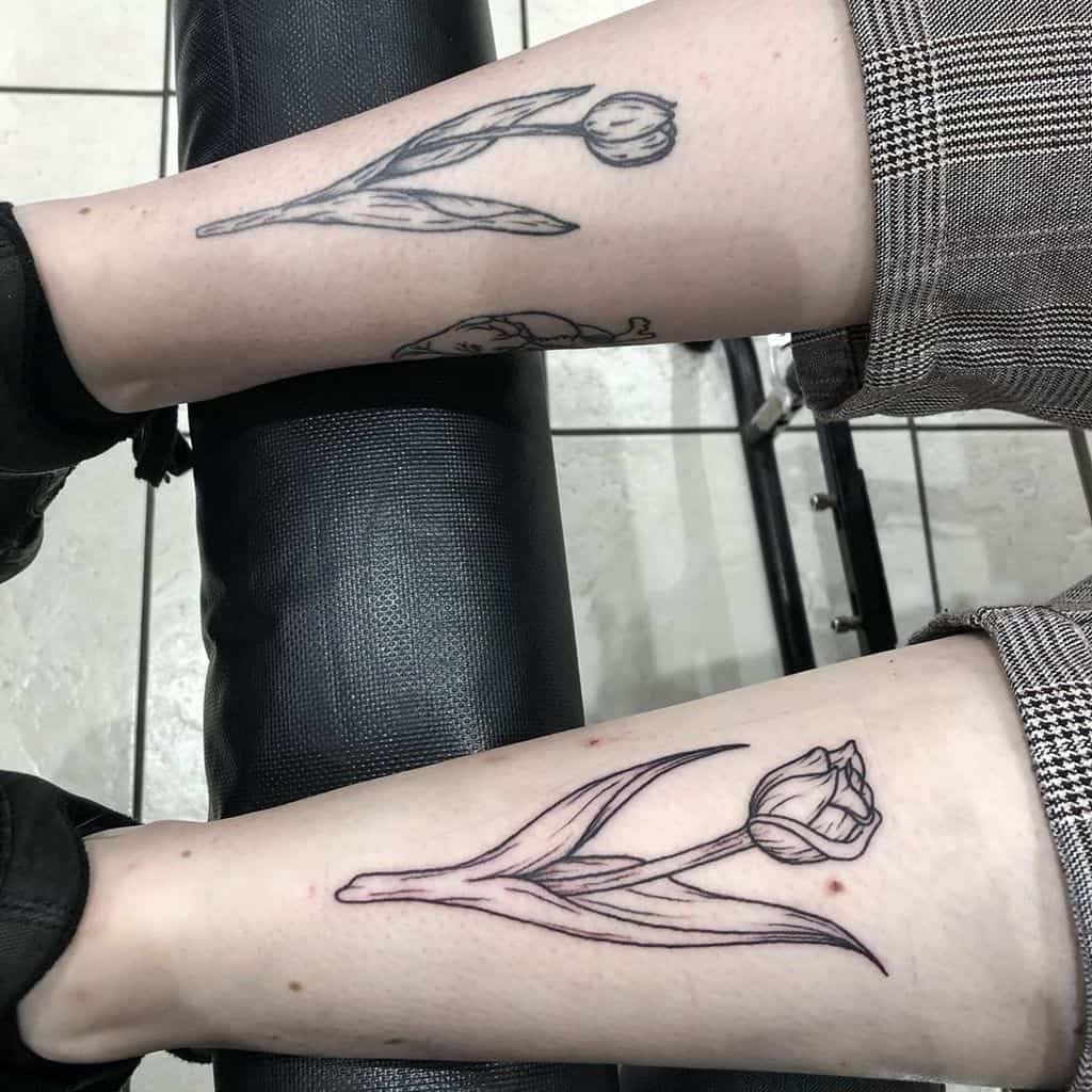 Two black-line tulip tattoos on the lower legs, featuring simple yet elegant floral designs with fine detailing and clean outlines.
