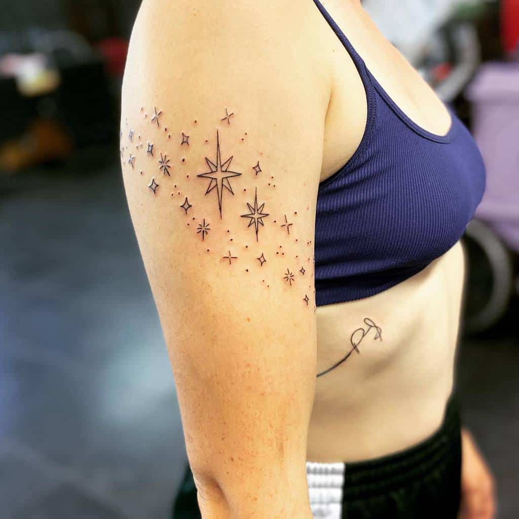 A minimalist tattoo on the upper arm featuring a cluster of delicate stars and dots, arranged in a flowing, celestial design