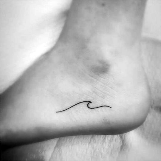 Minimalist wave tattoo in black ink on the inside of an ankle