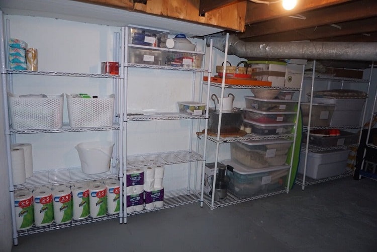 Simple basement storage with metal shelves, plastic bins, and wooden furniture in an unfinished space.
