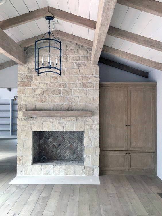 Rustic white stone fireplace with a wood mantel and herringbone firebox.
