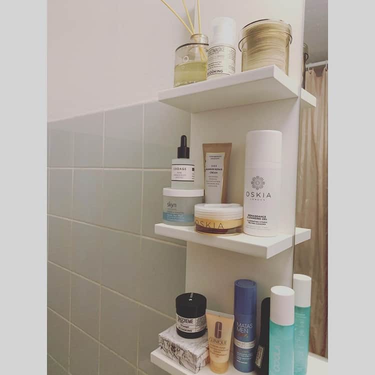 White bathroom shelf with skincare products and a candle.