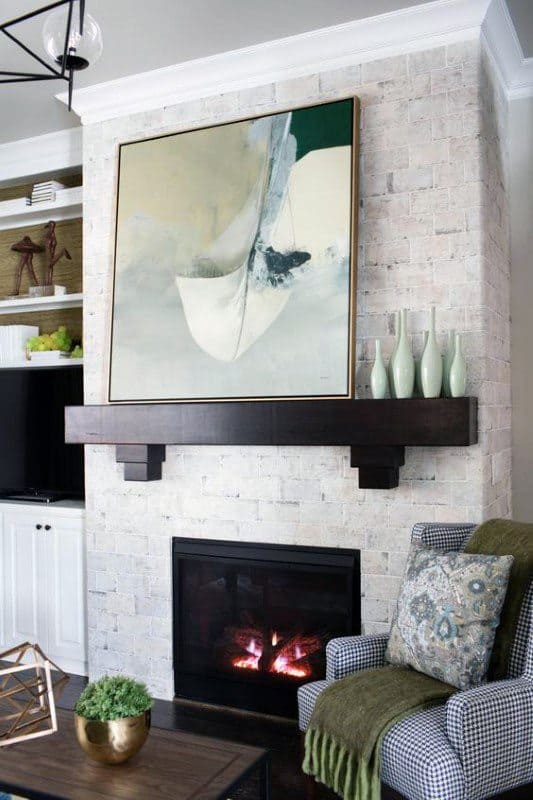 White brick fireplace with dark wood mantel, abstract artwork, and modern decorative vases.