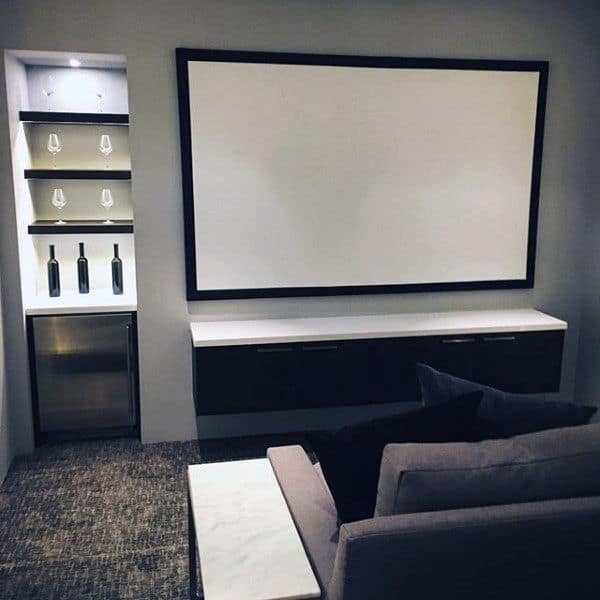 Home theater room with a large screen and a mini-bar with wine glasses and bottles, cozy seating area in front