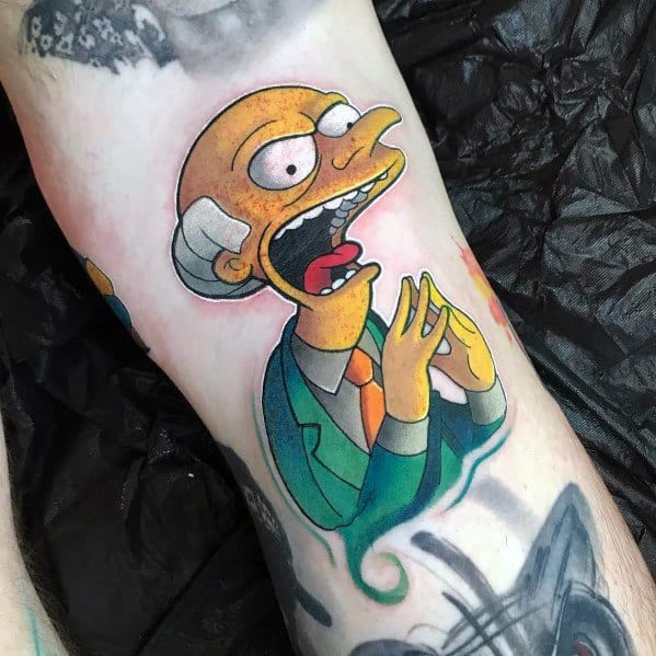 Colorful tattoo of Mr. Burns from The Simpsons with a sinister grin, rubbing his hands together in his iconic 'excellent' pose.