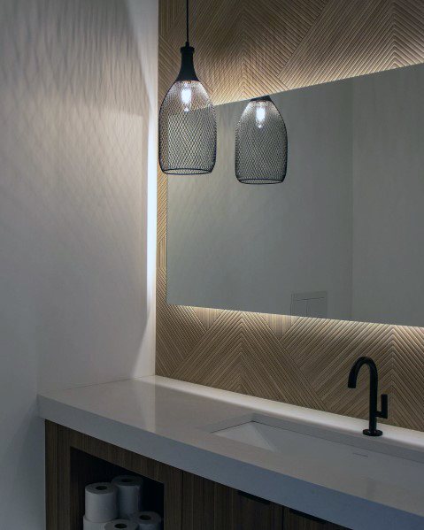 Minimalist bathroom with backlit mirror, herringbone accent wall, and wrought iron mesh pendant lights.