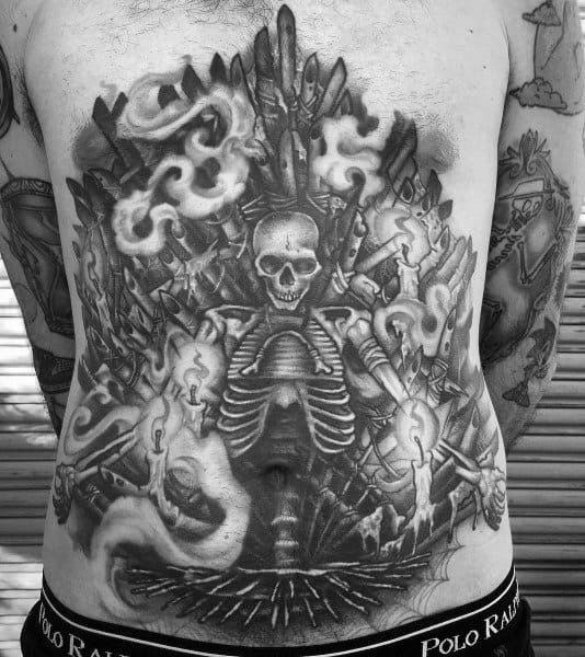 Black and gray full-back tattoo featuring a detailed skeleton sitting on a throne of swords, surrounded by flames and smoke, inspired by pirate lore.