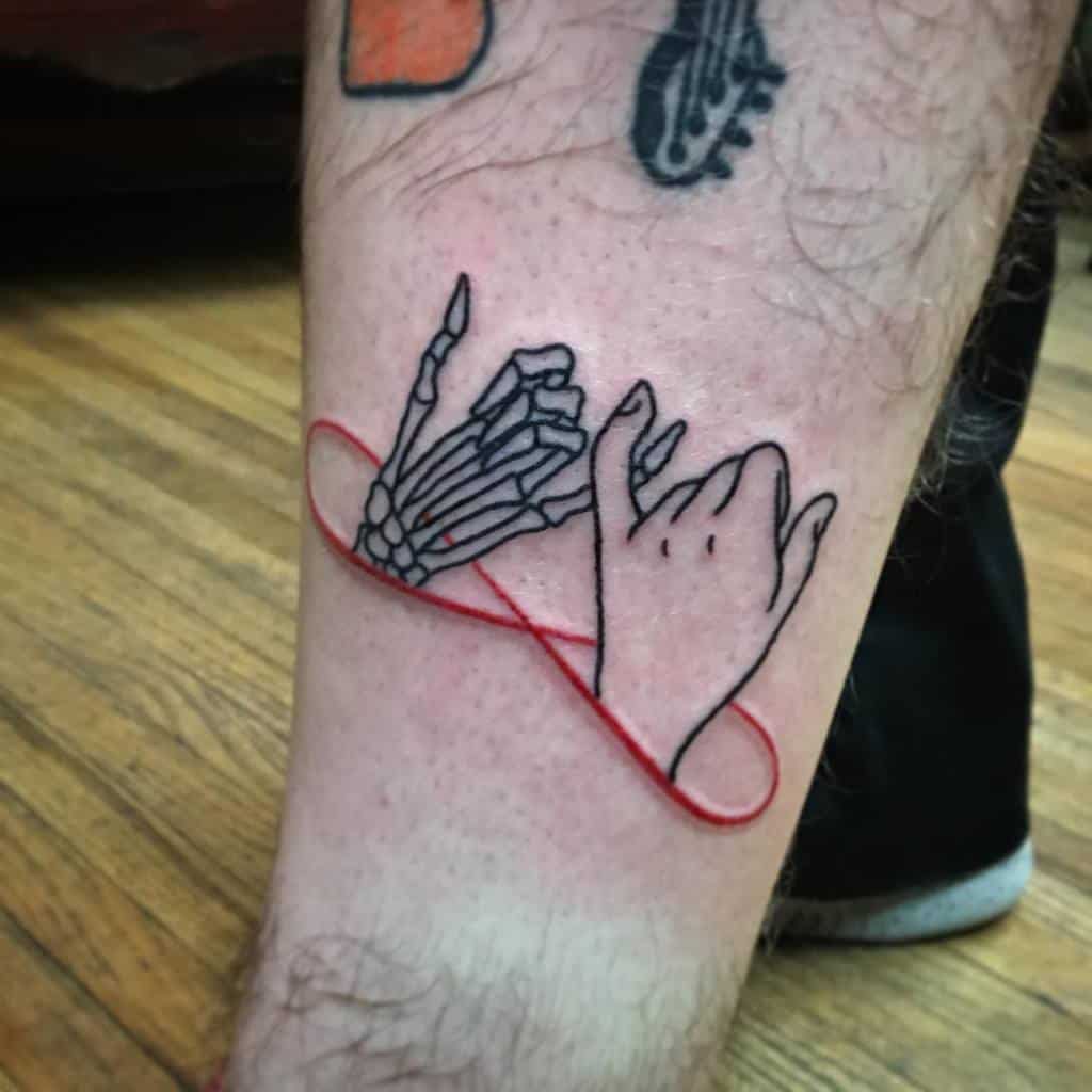 Tattoo of a hand and skeletal hand linked by a red infinity symbol on a person's leg