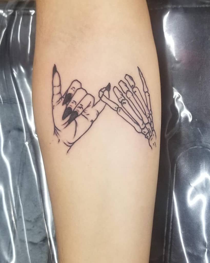 Tattoo of two hands making a pinky promise, with one hand as a skeleton and the other with long, painted nails