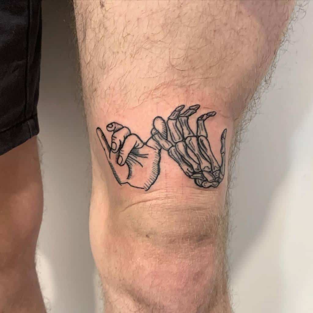 Tattoo of a human hand and a skeleton hand touching pinky fingers on a thigh