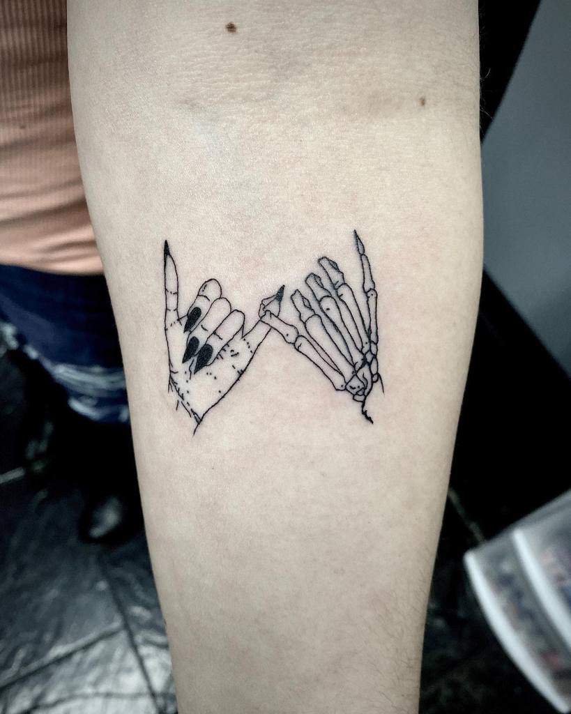 Tattoo of a hand and a skeleton hand interlocking pinky fingers on a  forearm