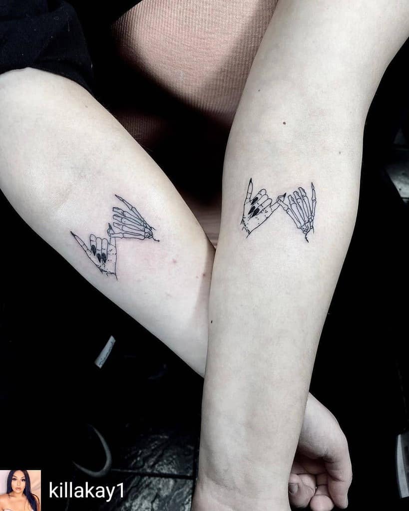 Matching pinky promise tattoos of a human hand and a skeleton hand with intricate details, placed on the inner forearms of two individuals