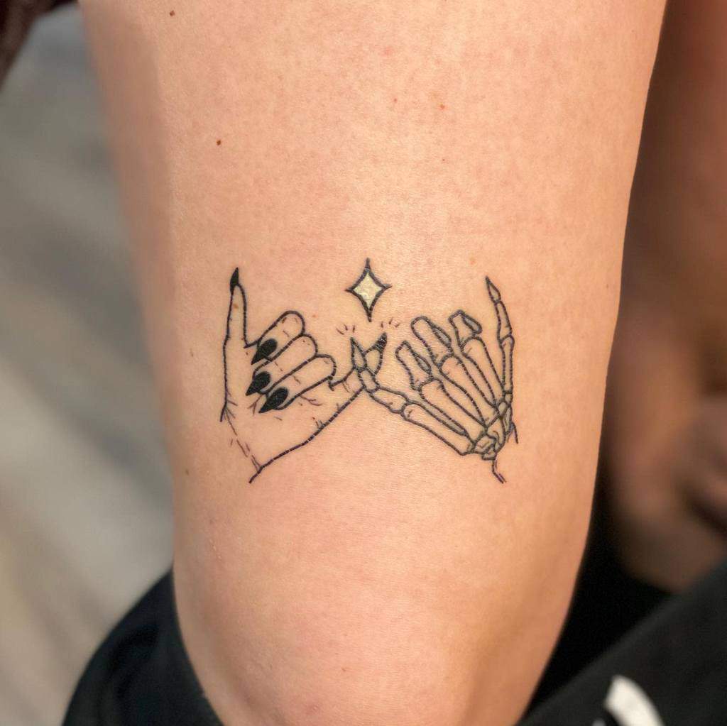 Tattoo of two pinky fingers linking, one skeleton and one human, with a small spark in between on a leg