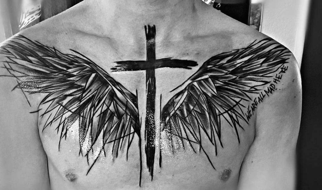 A black and white tattoo of a cross with angel wing-like designs with text 'We are all mad here'