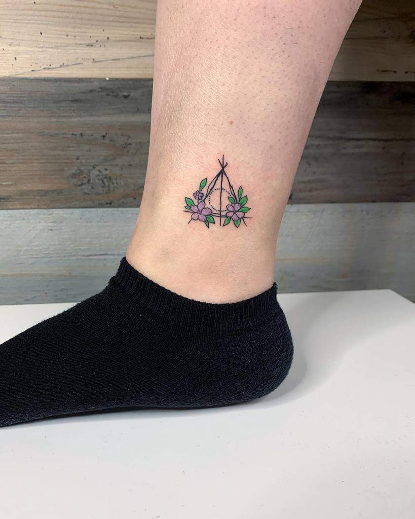 Minimalist Deathly Hallows tattoo with delicate floral accents in green and purple