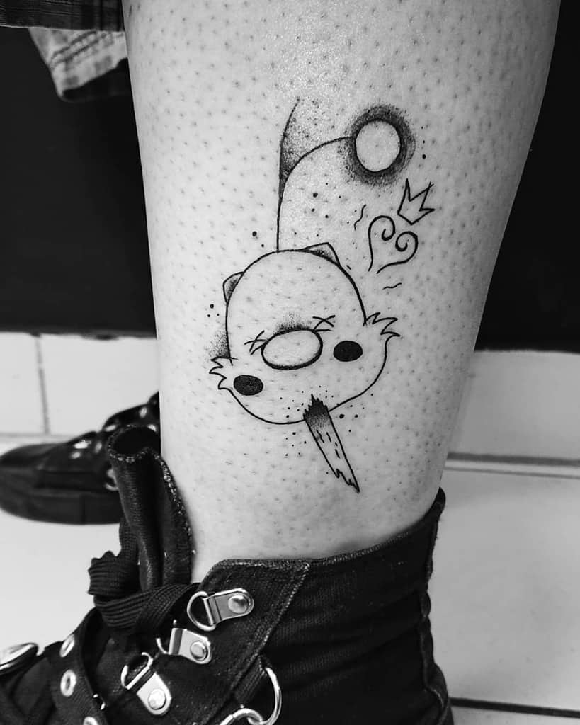 Minimalist black ink tattoo of Moogle from Kingdom Hearts with a heart, crown, and pom-pom, placed on the lower leg.