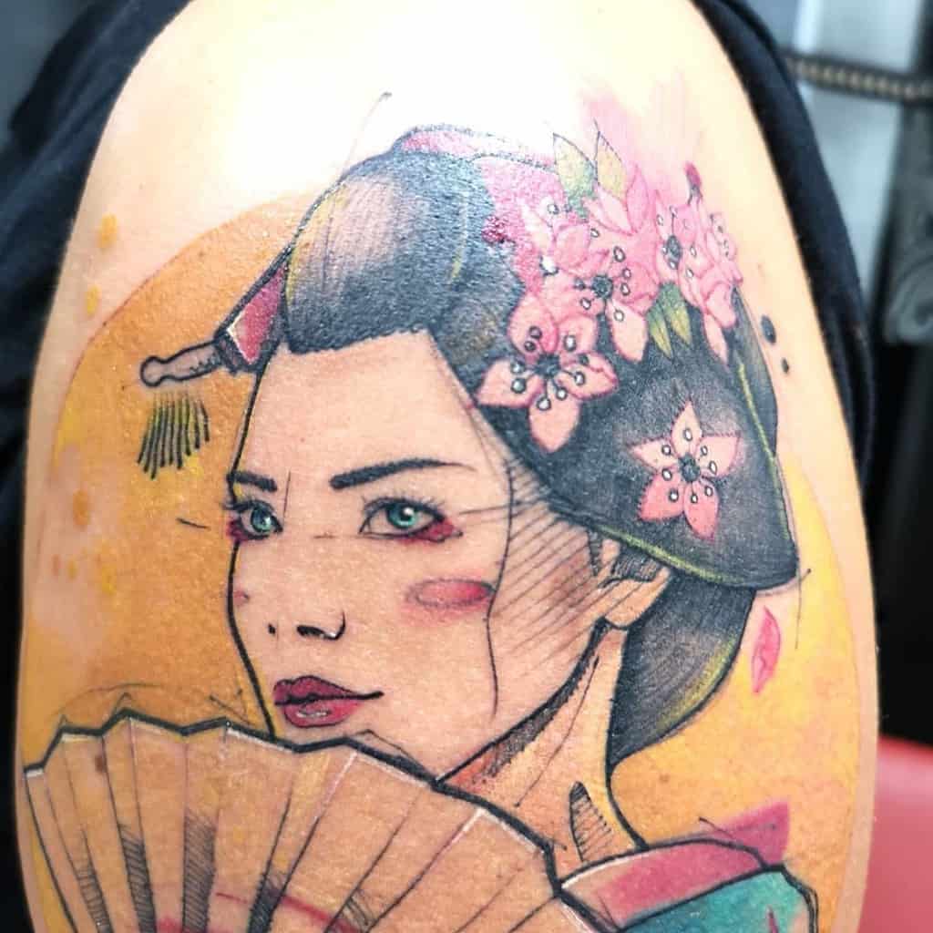 Vibrant tattoo of a Geisha with green eyes, floral hair ornaments, a hand fan, and a warm yellow background in a watercolor style.