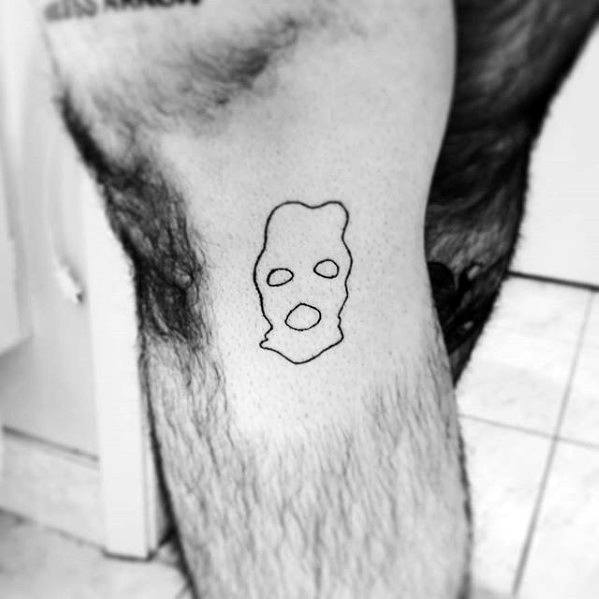 Minimalist ski mask tattoo with a simple black outline of eye and mouth holes, placed on the upper thigh.
