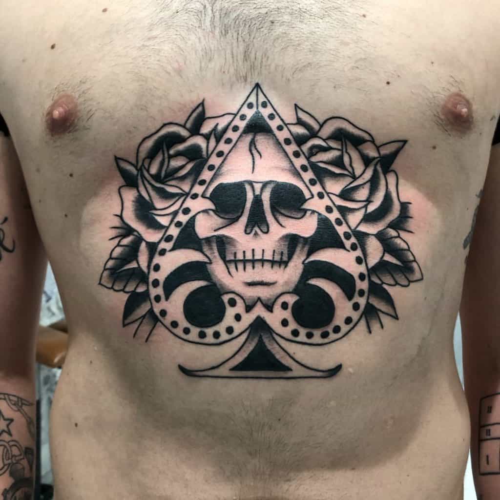 A bold black-and-white tattoo of the Ace of Spades symbol, with a skull in the center and surrounded by roses