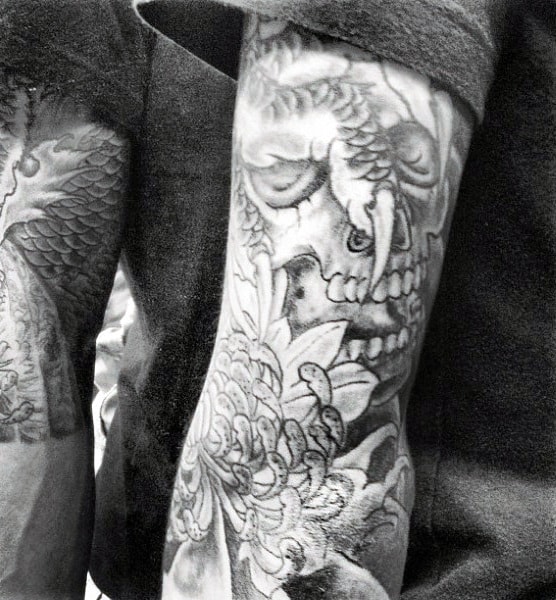 Black and white tattoos on an arm featuring a skull and floral design