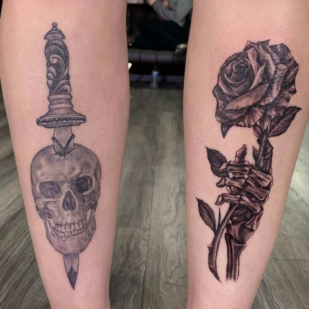 Black and grey leg tattoos featuring a skull impaled by a dagger on one leg and a skeletal hand holding a rose on the other, symbolizing life and death.
