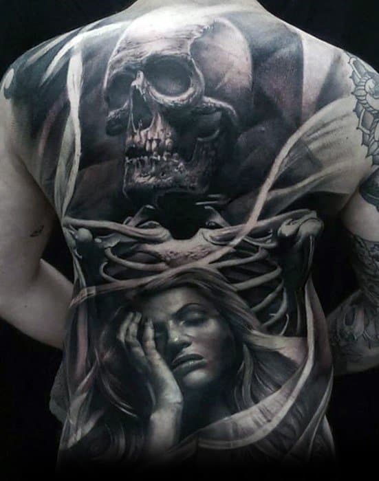 Emotive back tattoo featuring a detailed skull and ribcage above a peaceful woman’s face, blending life, death, and dreamlike serenity.