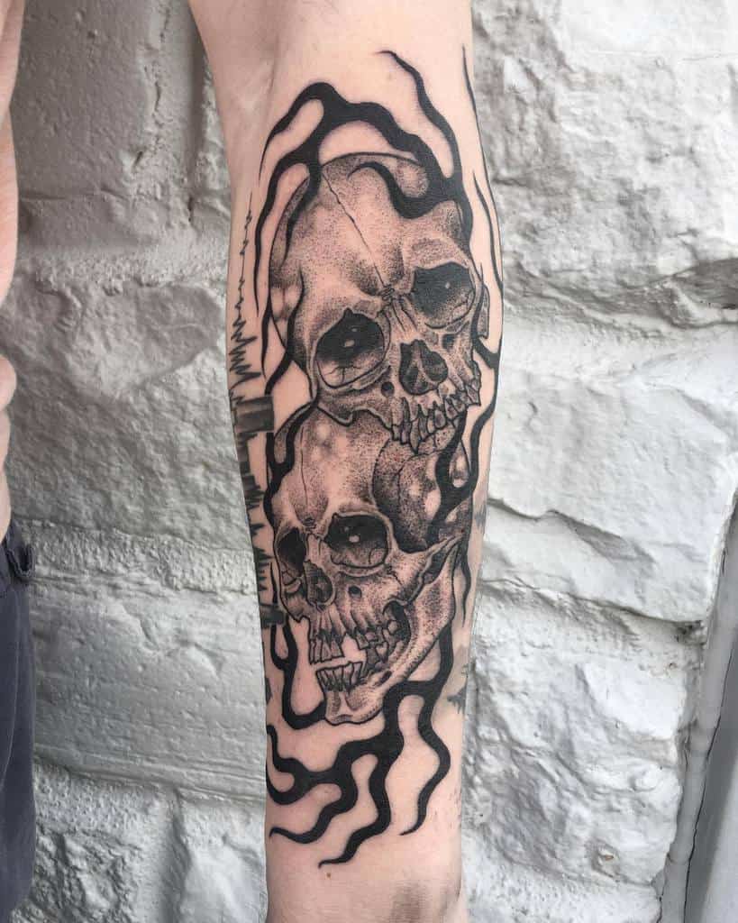 Tattoo of two skulls entwined with black flames on an arm