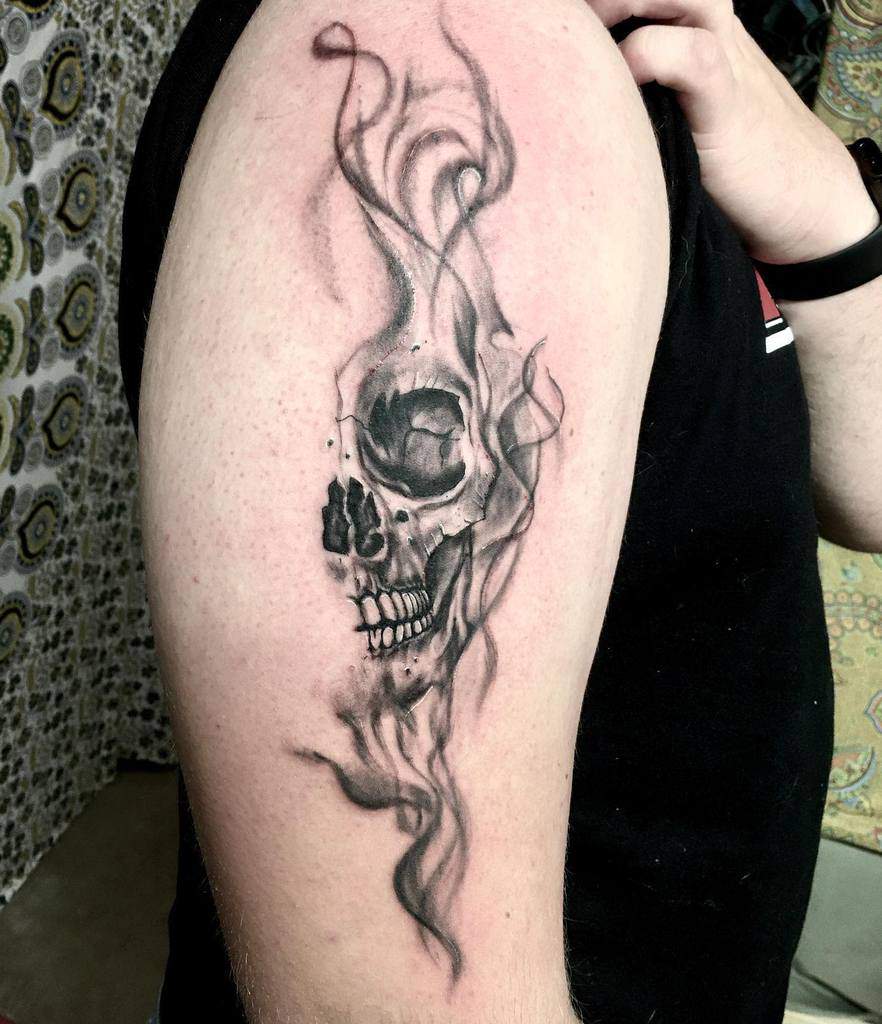 A tattoo of a smoky, stylized skull design on an upper arm