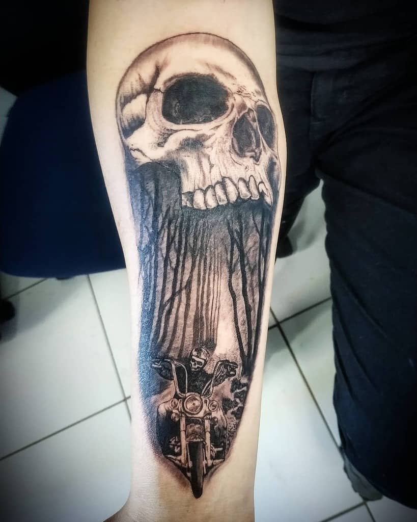 Tattoo of a skull with open mouth transforming into a motorcyclist on the arm in black and white