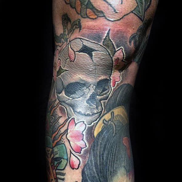 Bold knee tattoo featuring a cracked skull intertwined with cherry blossoms, blending dark and vibrant tones for a striking 3D effect