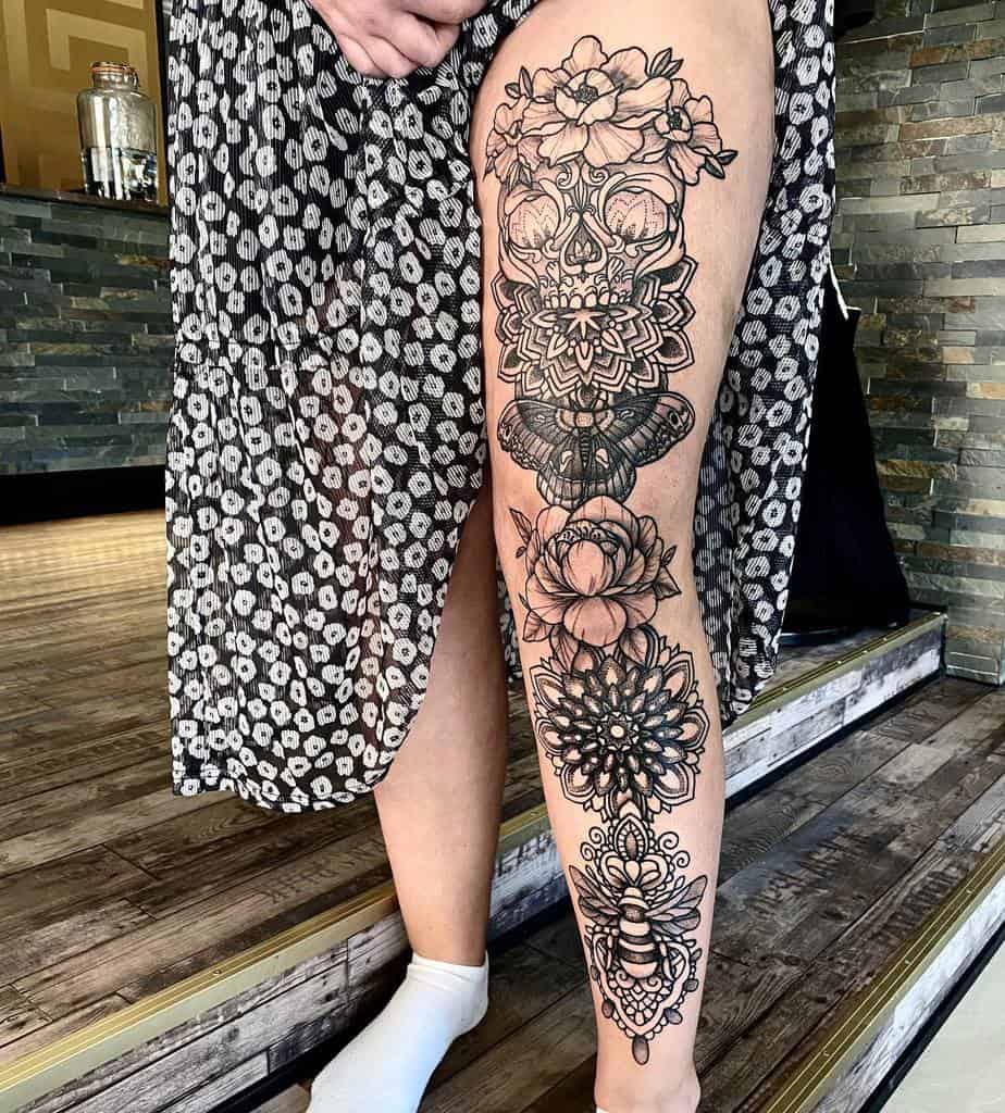 Black and grey tattoo leg sleeve featuring a floral skull with intricate patterns, a butterfly, bee and geometric mandala elements