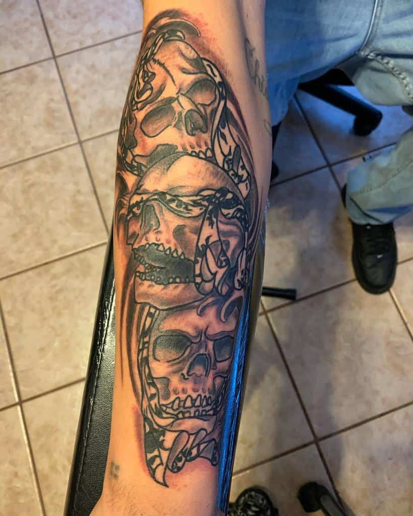 Black and gray tattoo of three skulls on a forearm, symbolizing 'Hear No Evil, See No Evil, Speak No Evil,' with intricate detailing and shading
